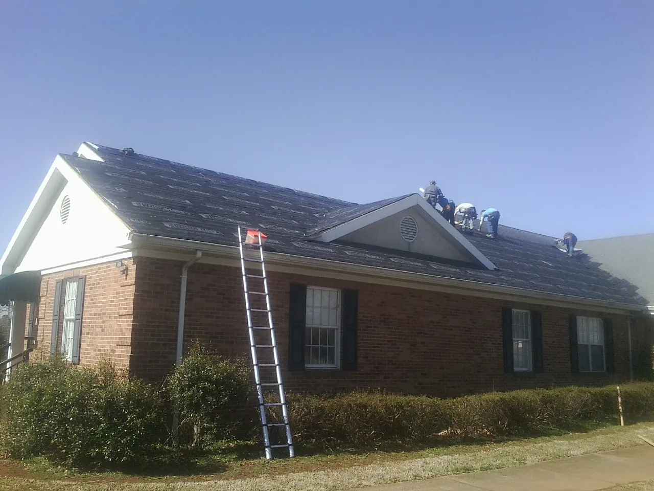 Crew tearing shingles off a brick ranch roof with a ladder set — Emergency Roof Repair work by our crew in Tampico