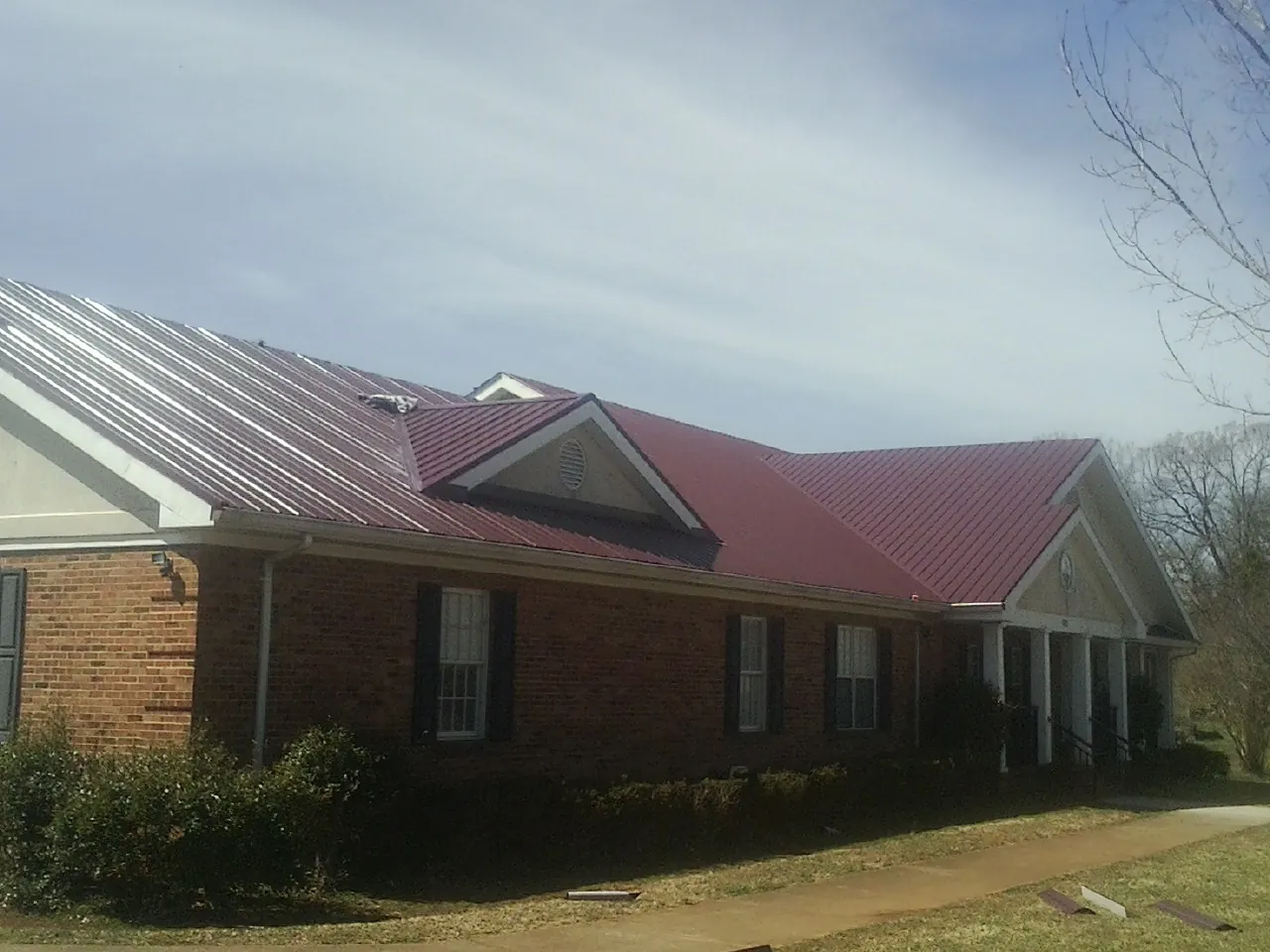 Red metal roof with gabled entries on a long brick building, from a Hail Damage Roof Repair job in Tampico