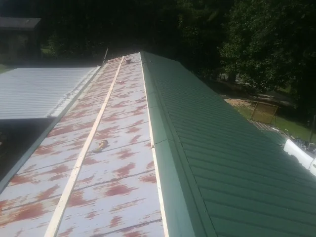 Old rusted panels beside newly installed green metal roofing — Wind Damage Roof Repair by Roofing Brothers in Tampico