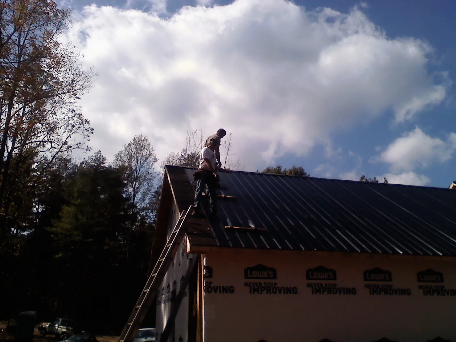 Roofer fastening dark metal panels high against a cloudy sky, from a Roof Inspection job in Tampico