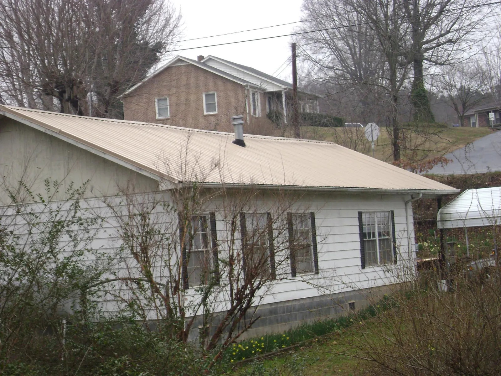 Tan metal roof on a white sided house set into a hillside — Commercial Roofing by Roofing Brothers in Tampico